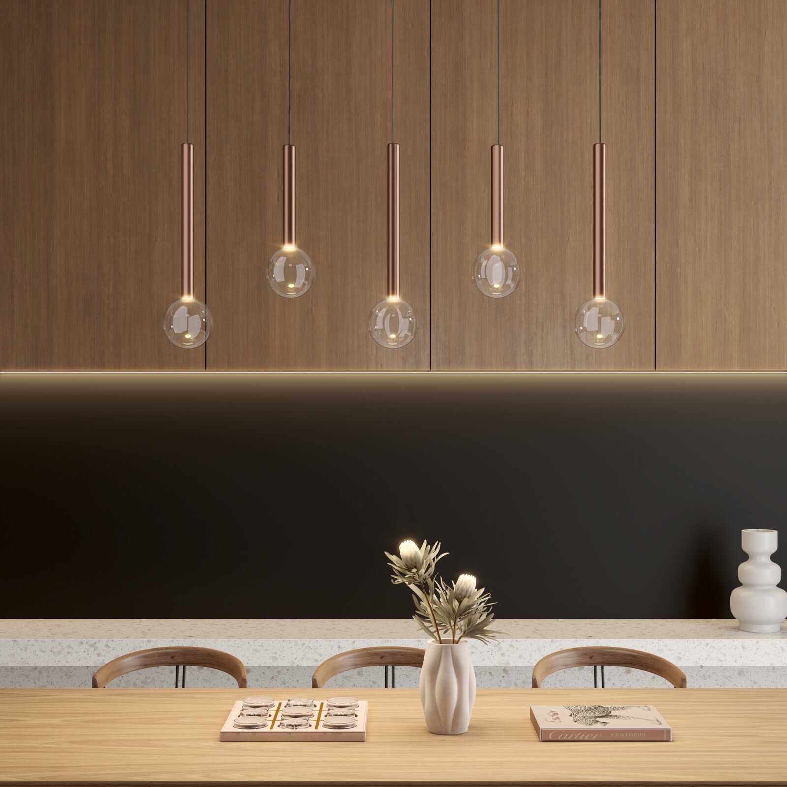 Moderne Pendelleuchten mit kupferfarbenen Röhren und klaren Glaskugeln vor Holzschränken über einem Esstisch mit Vase und Dekoration, Frontalansicht