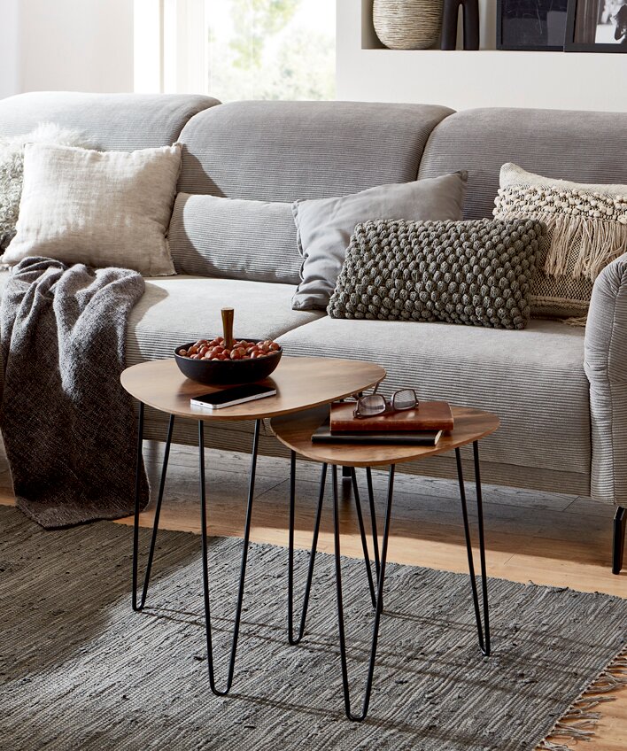 Zwei runde Beistelltische im Set mit Holzplatte und schwarzen Hairpin-Metallbeinen auf grauem Teppich vor einem hellgrauen Sofa, perspektivisch in leichter Schrägansicht von vorn.