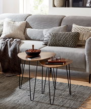 Zwei runde Beistelltische im Set mit Holzplatte und schwarzen Hairpin-Metallbeinen auf grauem Teppich vor einem hellgrauen Sofa, perspektivisch in leichter Schrägansicht von vorn.