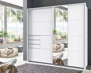 Moderner weißer Schwebetürenschrank mit Spiegel, frontale Ansicht in einem hellen Raum mit großen Fenstern.