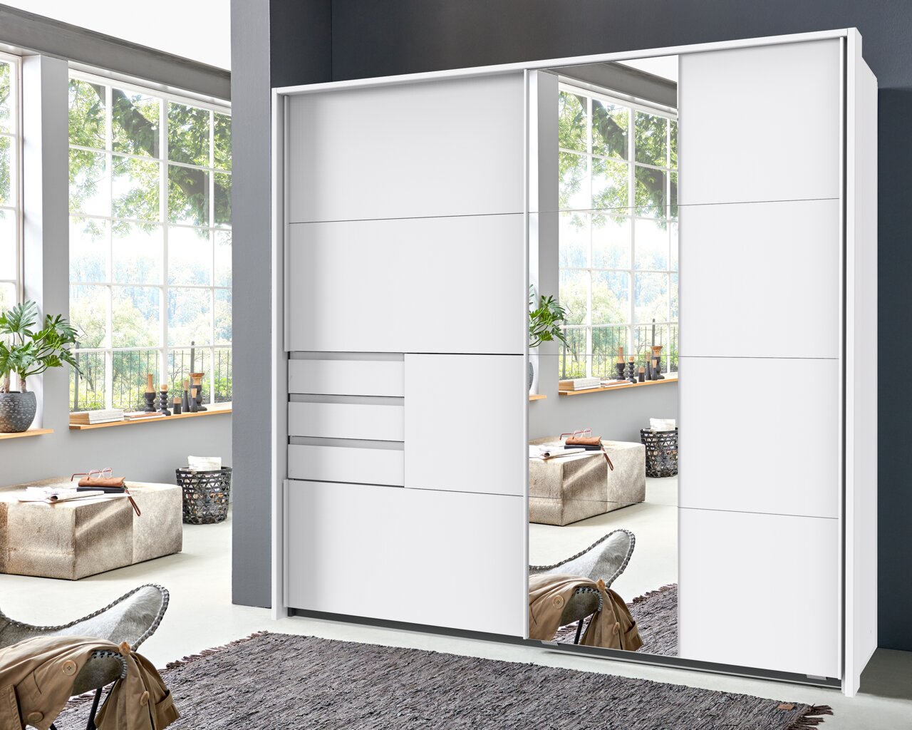Moderner weißer Schwebetürenschrank mit Spiegel, frontale Ansicht in einem hellen Raum mit großen Fenstern.