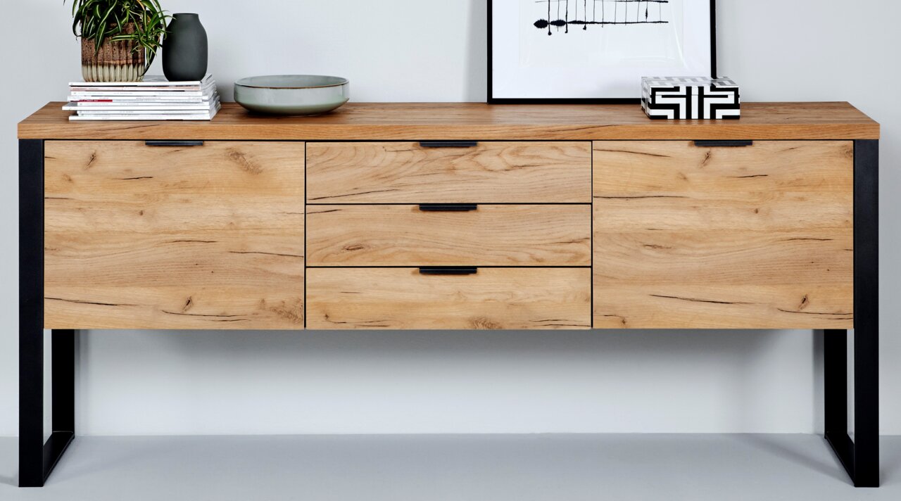 Vooraanzicht van een modern houten dressoir met zwarte metalen poten, versierd met planten en kunstvoorwerpen.