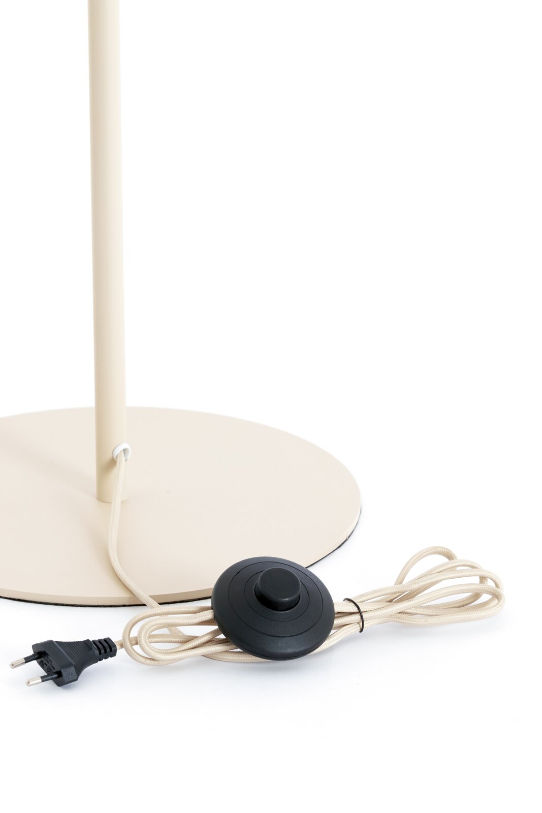 Detailaanzicht van onderen van een crèmekleurige vloerlamp met ronde voet, textielsnoer, zwarte voetschakelaar en Europese stekker