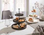 Zwei Etageren aus Porzellan, eine in Schwarz und eine in Weiß, auf einem gedeckten Tisch mit Snacks und Weingläsern, seitliche Perspektive.