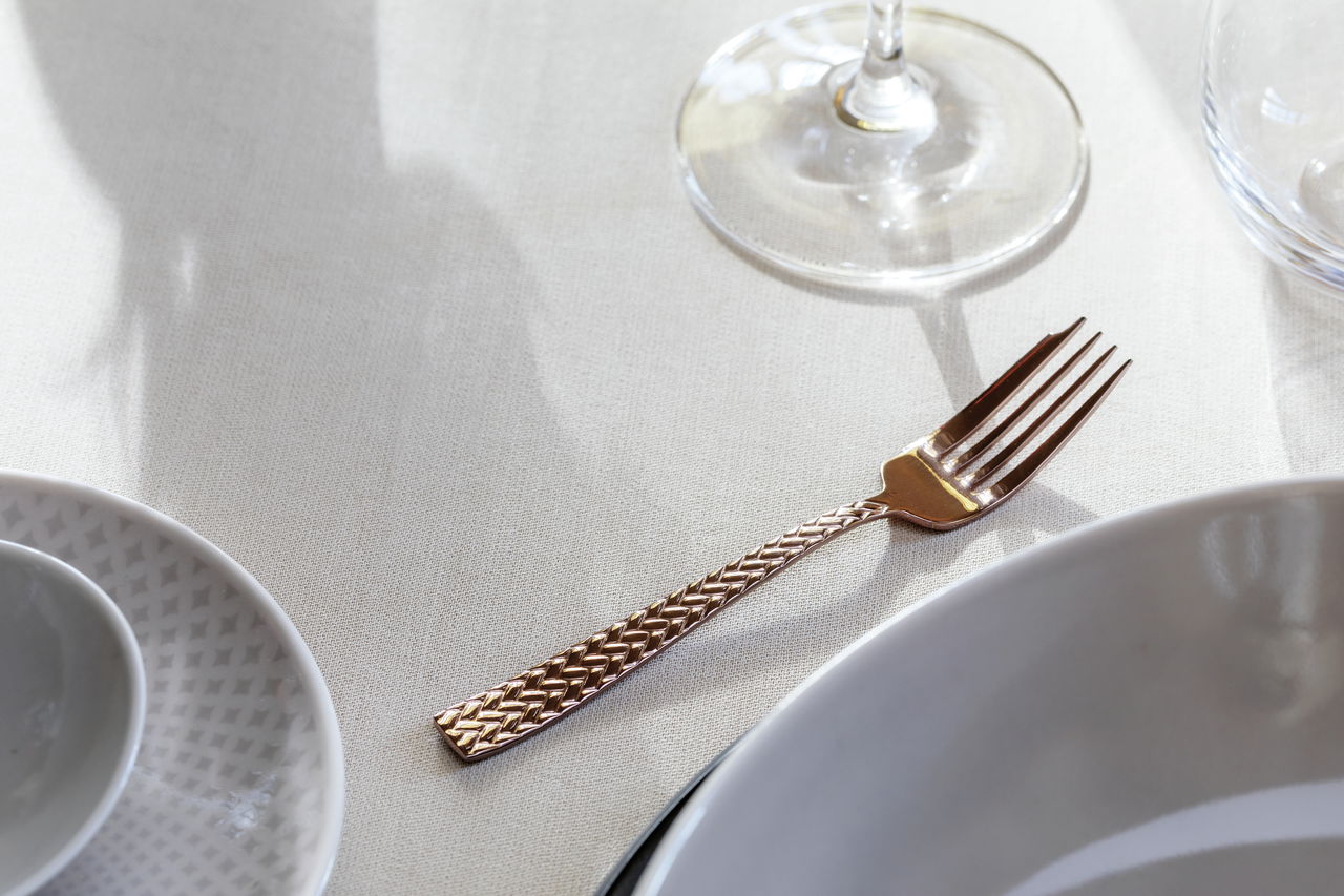 Kupferfarbene Gabel des Bestecksets Cortina auf einem gedeckten Tisch, seitliche Perspektive.