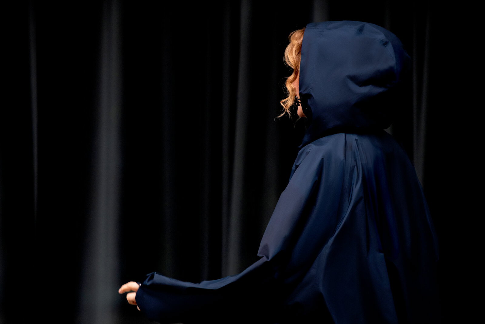 Dunkelblauer Kapuzenmantel/Umhang an einer Person, seitliche Profilansicht von rechts vor dunklem Hintergrund