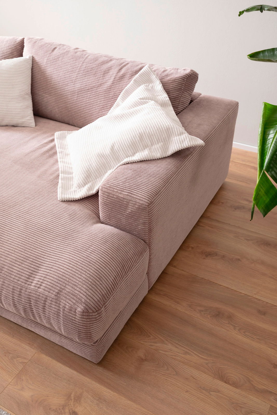 Nahaufnahme eines kleinen Megasofas in rosa Cordstoff mit weißen Kissen, von schräg oben fotografiert.