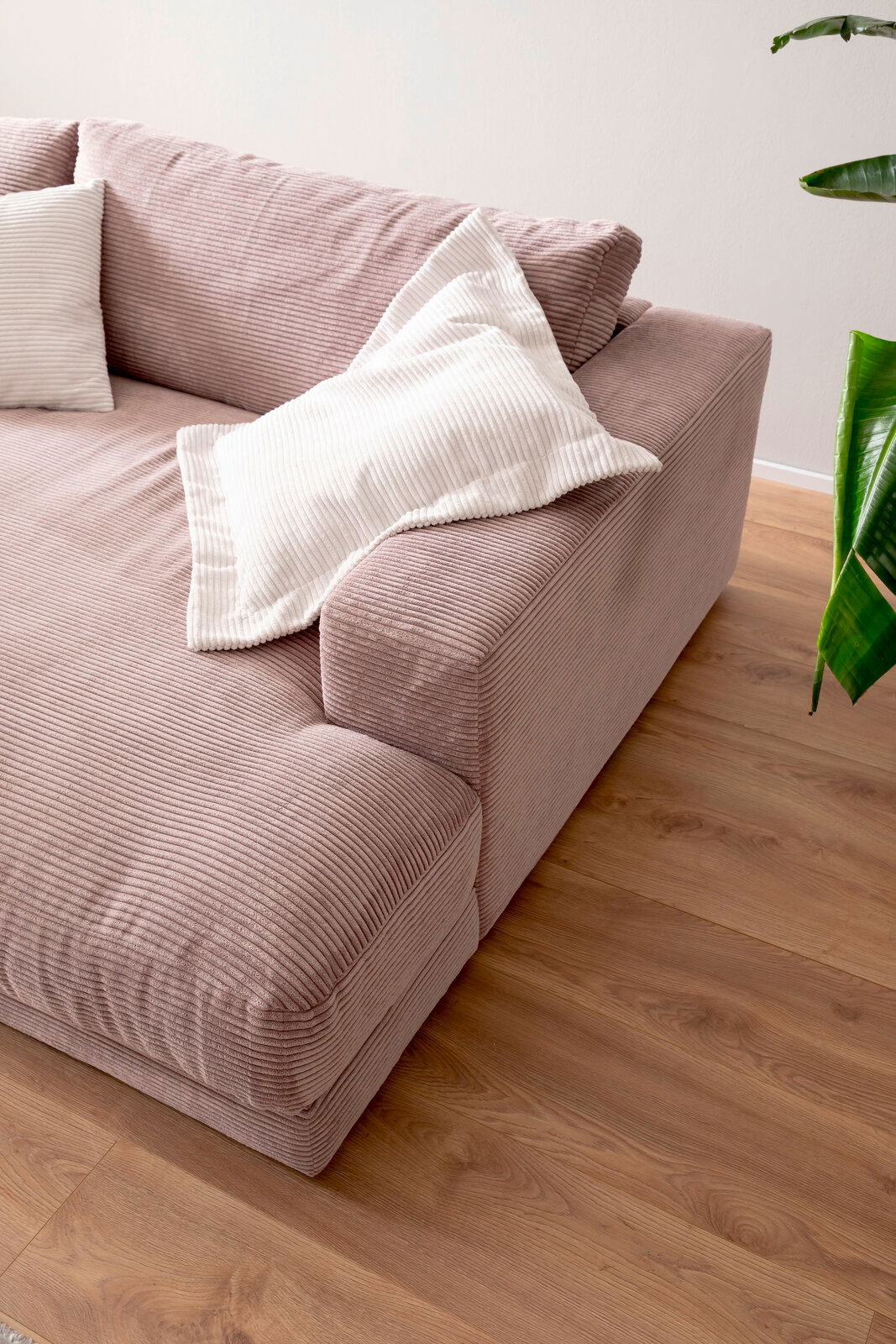 Nahaufnahme eines kleinen Megasofas in rosa Cordstoff mit weißen Kissen, von schräg oben fotografiert.