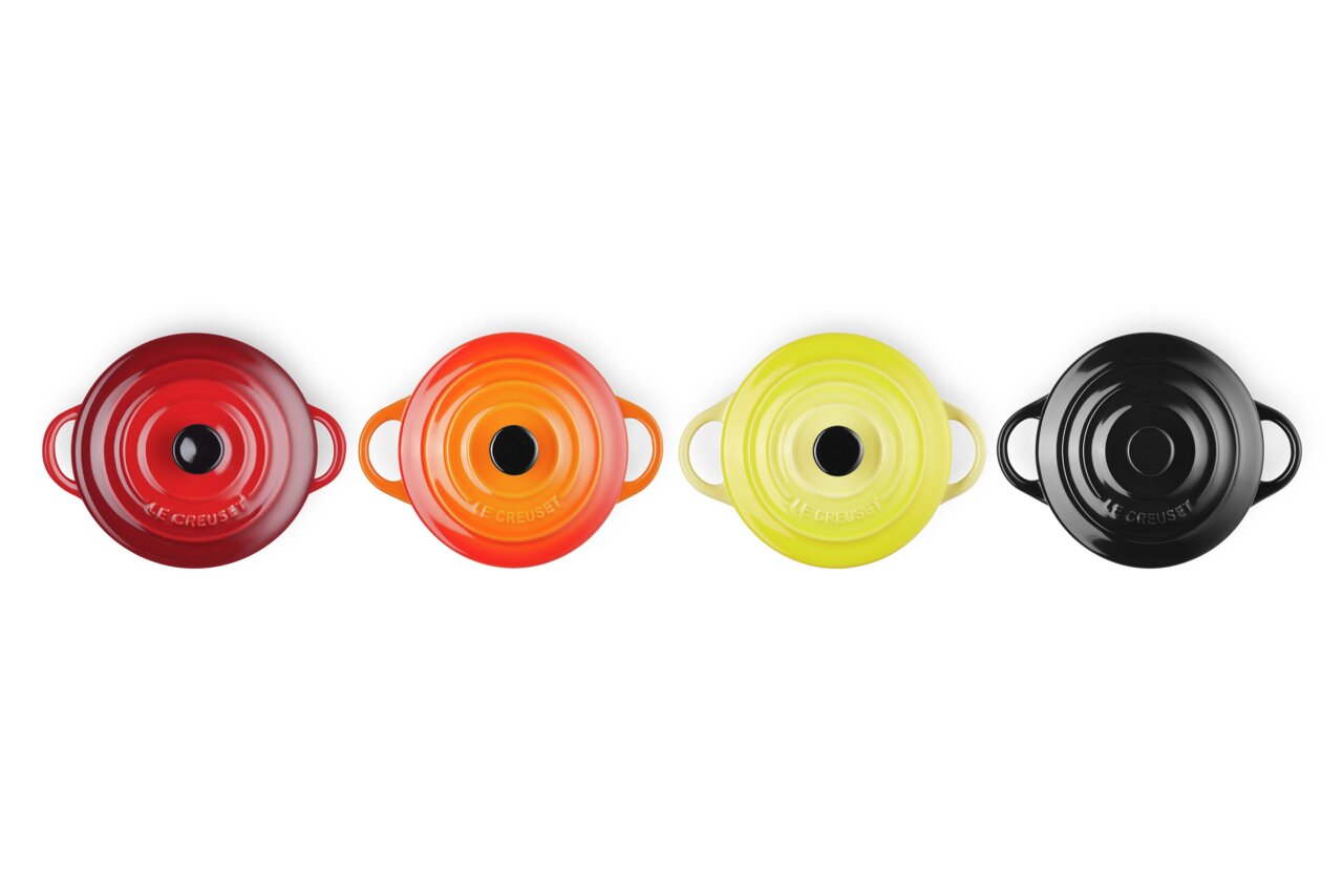 LE CREUSET Mini-Cocotte 4er-Set 10cm FEUER UND FLAMME Vier Mini-Cocottes in verschiedenen Farben (Rot, Orange, Gelb, Schwarz) aus der Vogelperspektive.