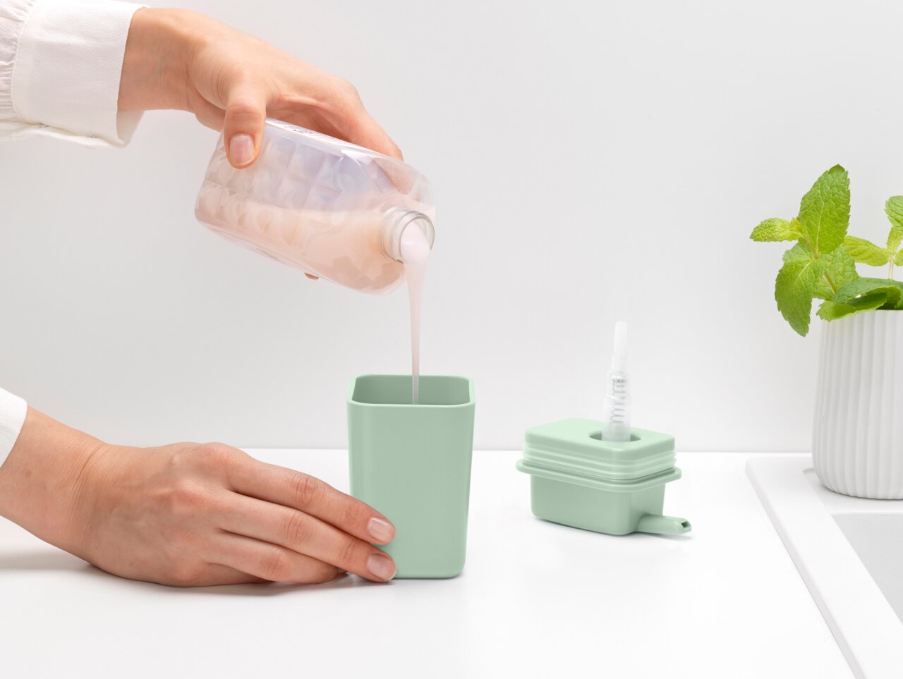 Een hand giet vloeibare zeep in een mintgroene zeepdispenser, gezien vanuit de zijkant.