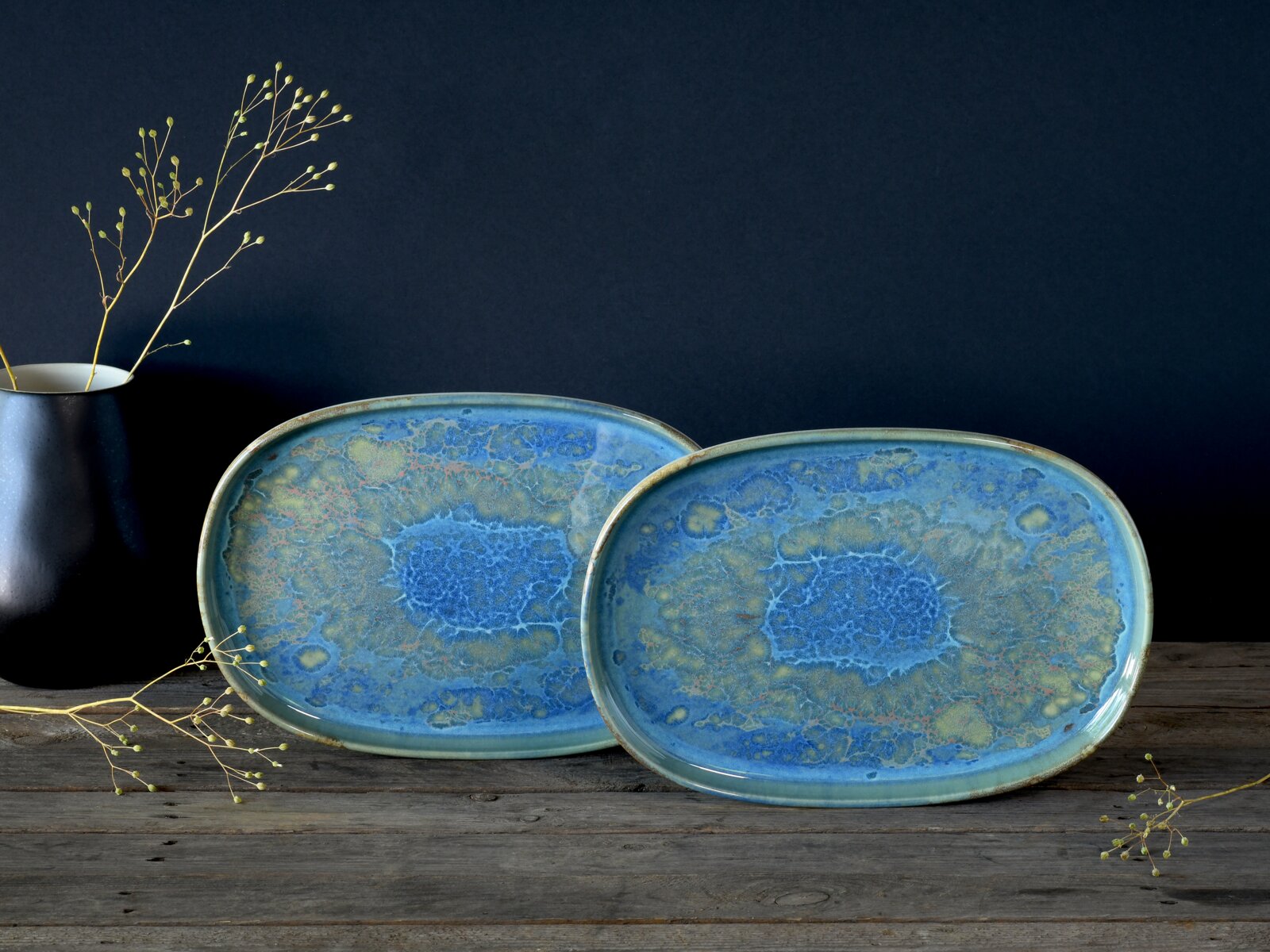 Zwei ovale Keramik-Servierplatten mit blau-grün marmorierter Glasur auf rustikalem Holztisch vor dunklem Hintergrund, frontal leicht von oben fotografiert.