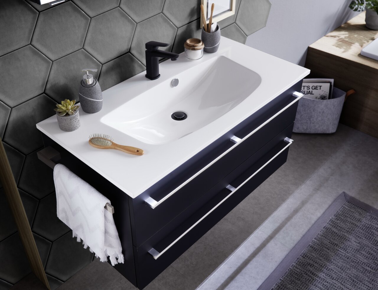Moderne Badkombination mit weißem Waschbecken und schwarzem Unterschrank, von oben fotografiert. Dekoriert mit Seifenspender, Pflanze und Handtuch.