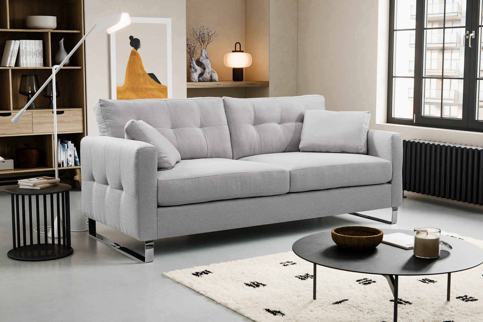Hellgraues, modern gepolstertes 3-Sitzer-Sofa mit Steppnähten und Chromfüßen im Wohnzimmer, Frontansicht leicht schräg von links