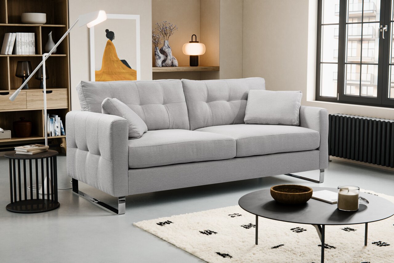 Hellgraues, modern gepolstertes 3-Sitzer-Sofa mit Steppnähten und Chromfüßen im Wohnzimmer, Frontansicht leicht schräg von links
