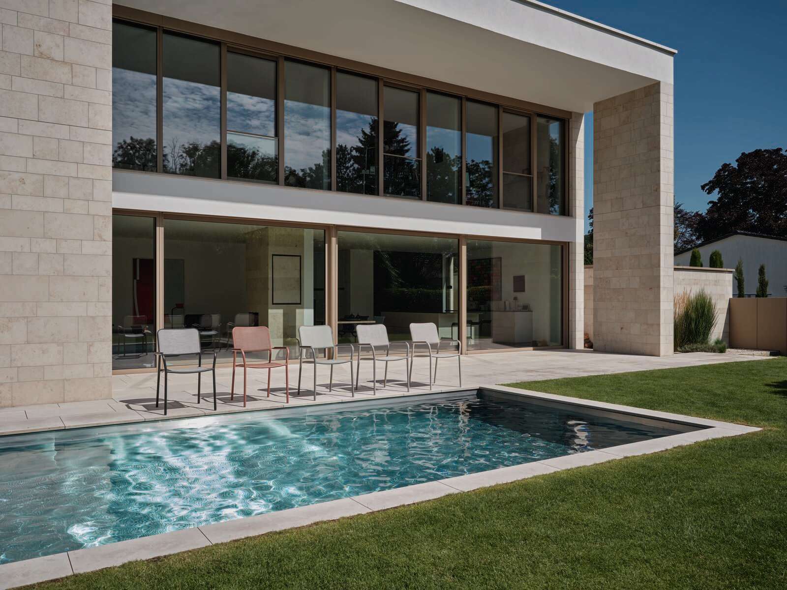 Mehrere Stapelsessel auf einer Terrasse mit Blick auf einen Pool und ein modernes Gebäude im Hintergrund.