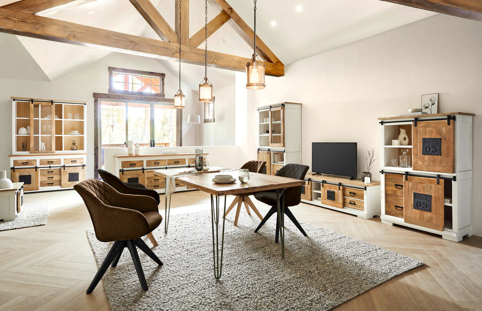 Wohnzimmer mit rustikalen Holzmöbeln, darunter Vitrine, Sideboard und Highboard, in einem hellen Raum mit Holzbalkendecke, aus der Perspektive von vorne betrachtet.