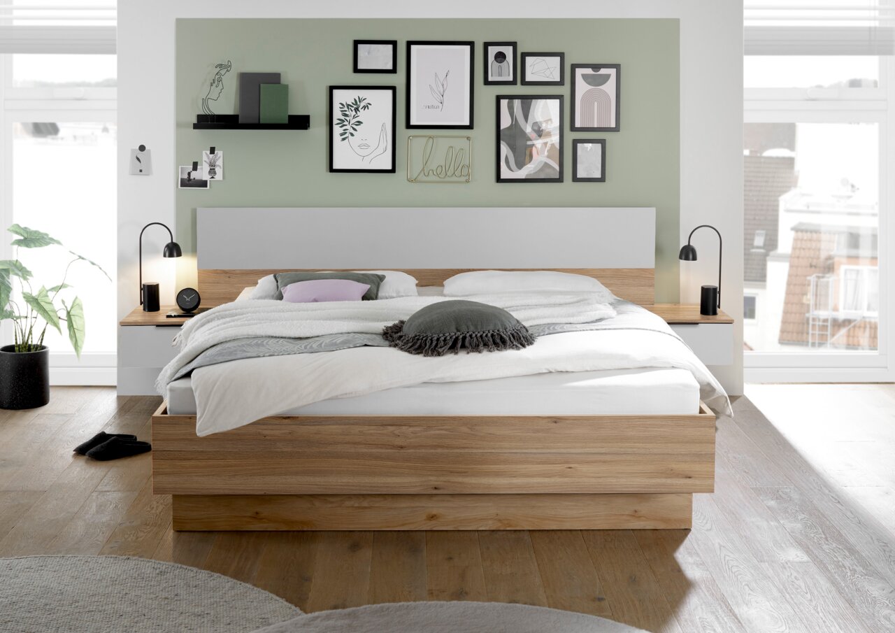 Modernes Schlafzimmer mit einem stilvollen Holzbett, umgeben von dekorativen Bildern an der Wand. Die Perspektive zeigt das Bett frontal mit Nachttischen und Lampen auf beiden Seiten.