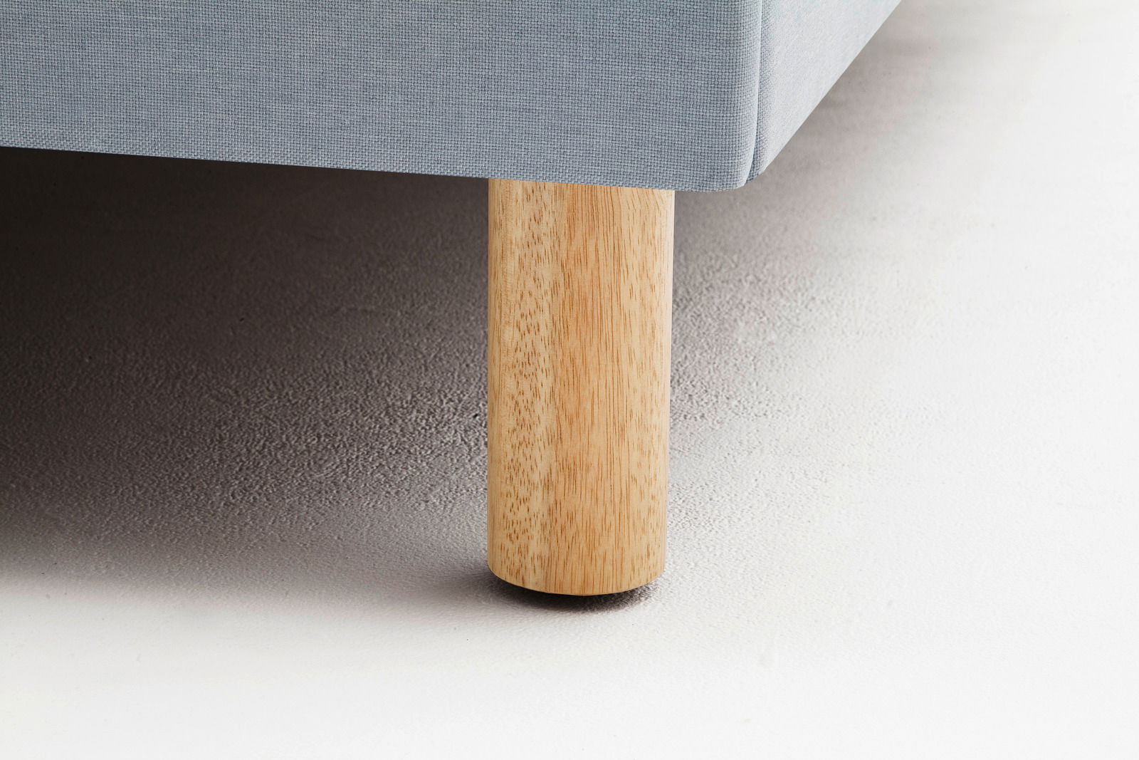 Nahaufnahme eines Polsterbettbeins aus hellem Holz mit grauem Stoffbezug, seitliche Perspektive.