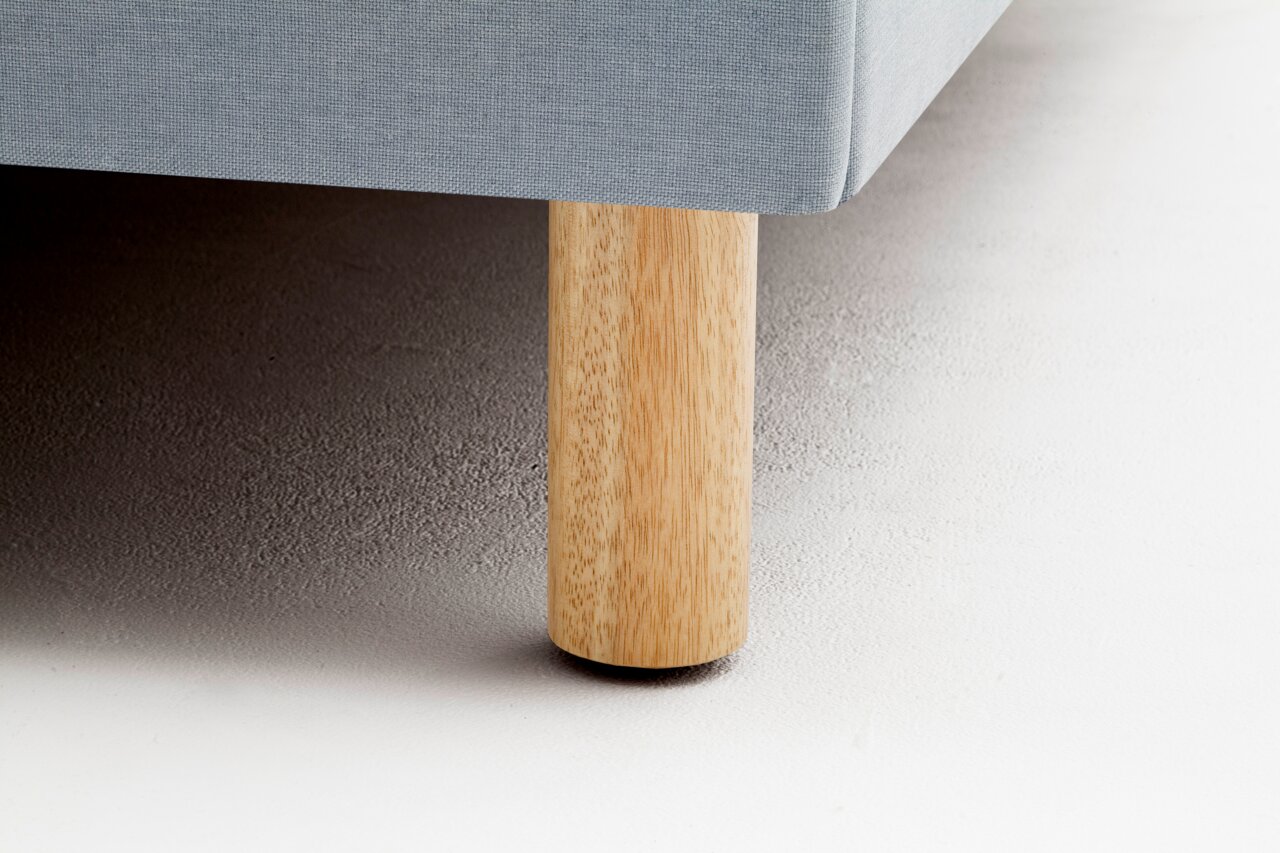 Nahaufnahme eines Polsterbettbeins aus hellem Holz mit grauem Stoffbezug, seitliche Perspektive.