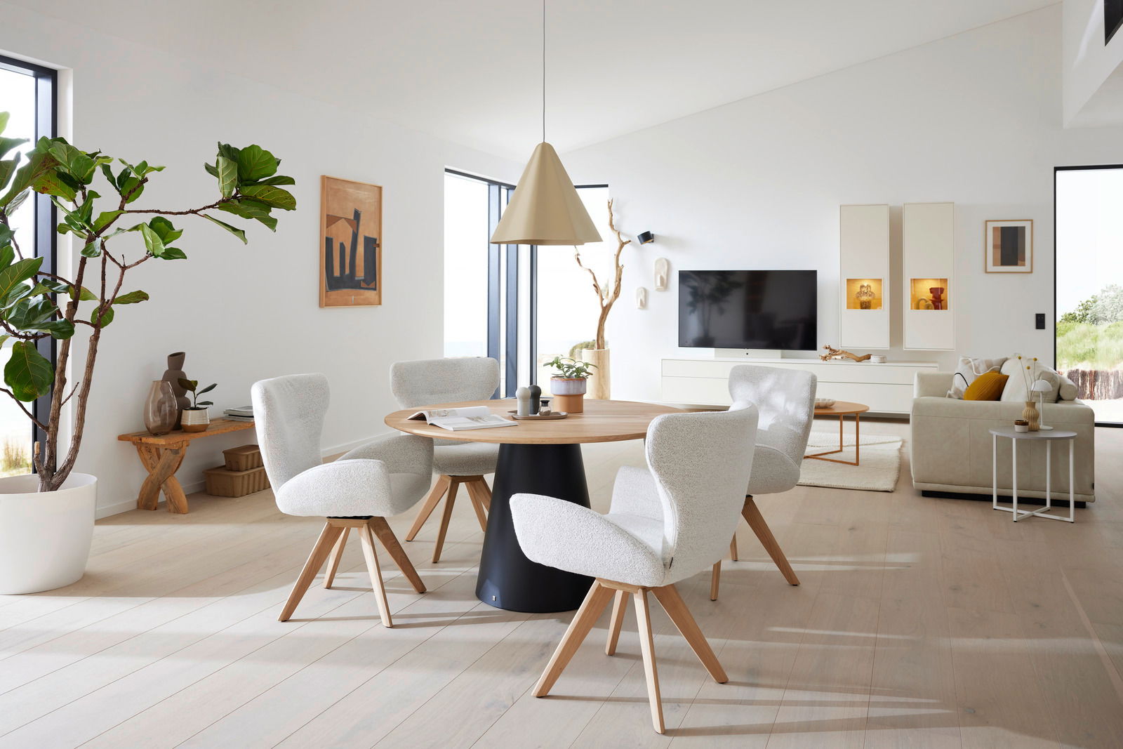 Moderner Essbereich mit rundem Holztisch und vier gepolsterten Armlehnstühlen in einem hellen, minimalistischen Wohnzimmer. Perspektive: seitlich von vorne.