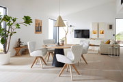 Moderner Essbereich mit rundem Holztisch und vier gepolsterten Armlehnstühlen in einem hellen, minimalistischen Wohnzimmer. Perspektive: seitlich von vorne.