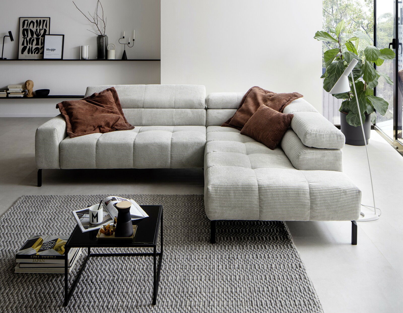 Moderne, graue Rundecke in L-Form mit braunen Kissen, in einem stilvoll eingerichteten Wohnzimmer mit Blick auf ein großes Fenster.