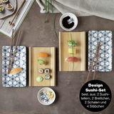 Sushi-Set mit blauen Blumenmustern, bestehend aus zwei rechteckigen Tellern, zwei Holzbrettchen, zwei Schalen und vier Essstäbchen, aus der Vogelperspektive fotografiert.