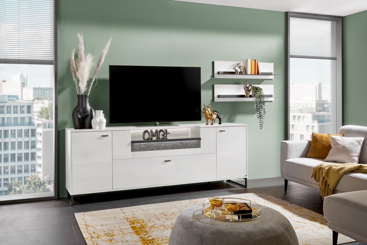 Set one by Musterring TV-Lowboard DELTONA Modernes weißes TV-Lowboard in einem stilvollen Wohnzimmer, frontal betrachtet, mit Dekorationen und einem großen Fernseher darauf.