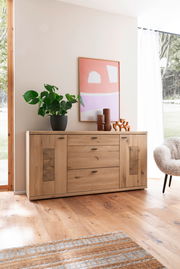 Holz-Sideboard mit drei Schubladen und zwei Türen, dekoriert mit Pflanzen und Vasen, in einem modernen Wohnzimmer aus der Frontalperspektive.