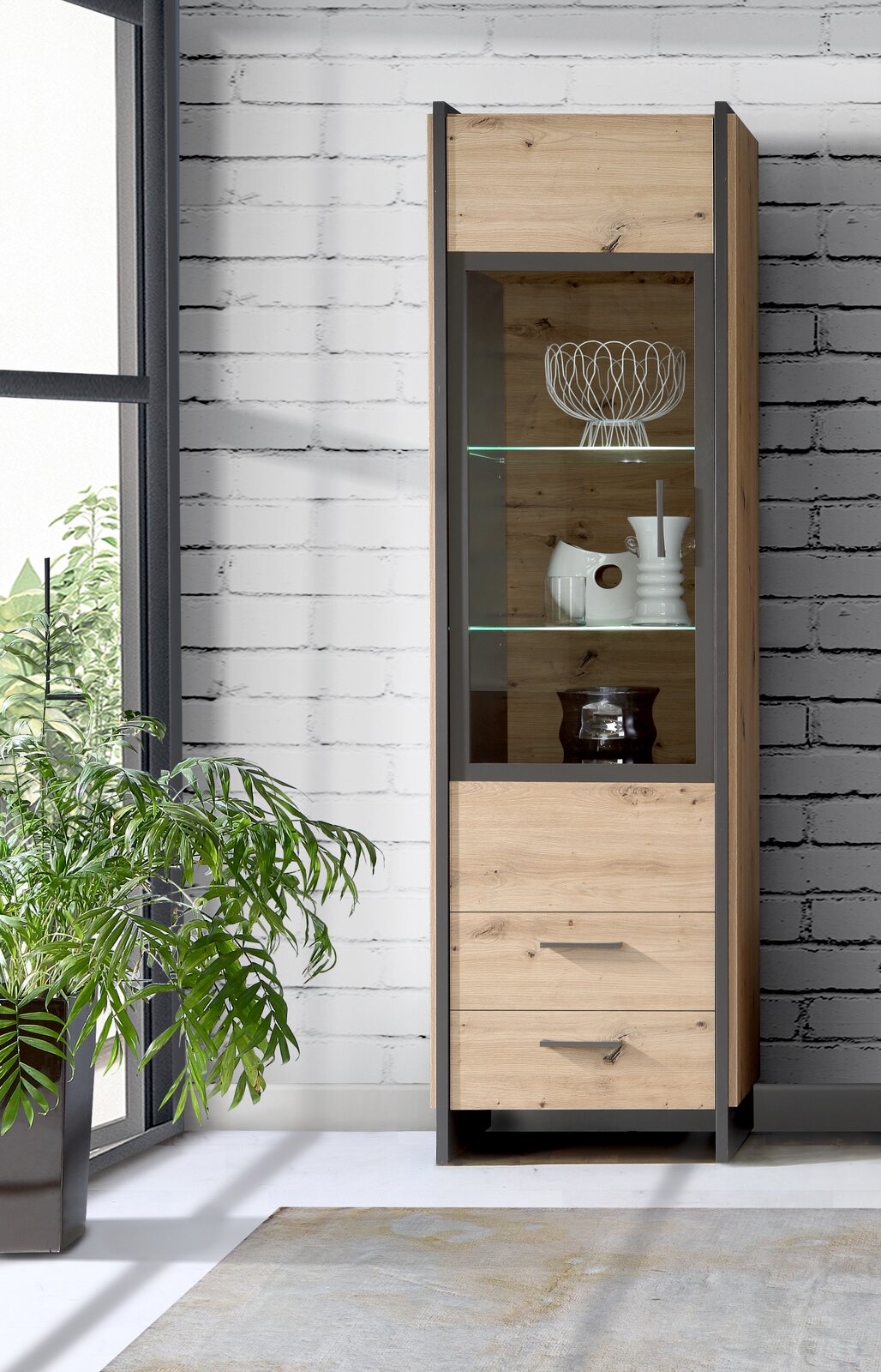 Moderne Vitrine aus Holz mit Glasfront, seitliche Perspektive, dekoriert mit Geschirr und Pflanzen im Hintergrund.