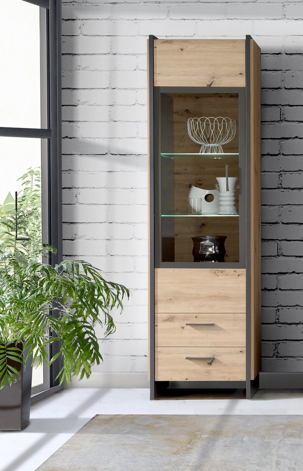 Moderne Vitrine aus Holz mit Glasfront, seitliche Perspektive, dekoriert mit Geschirr und Pflanzen im Hintergrund.