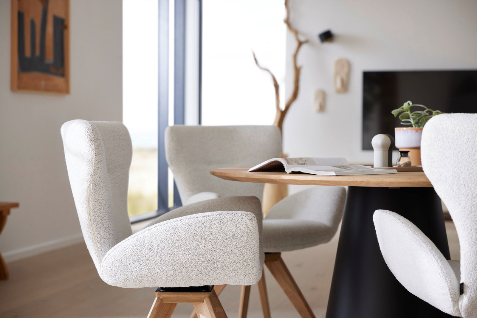 Moderner Armlehnstuhl in hellem Stoffbezug, seitliche Perspektive, neben einem runden Holztisch in einem stilvoll eingerichteten Raum.