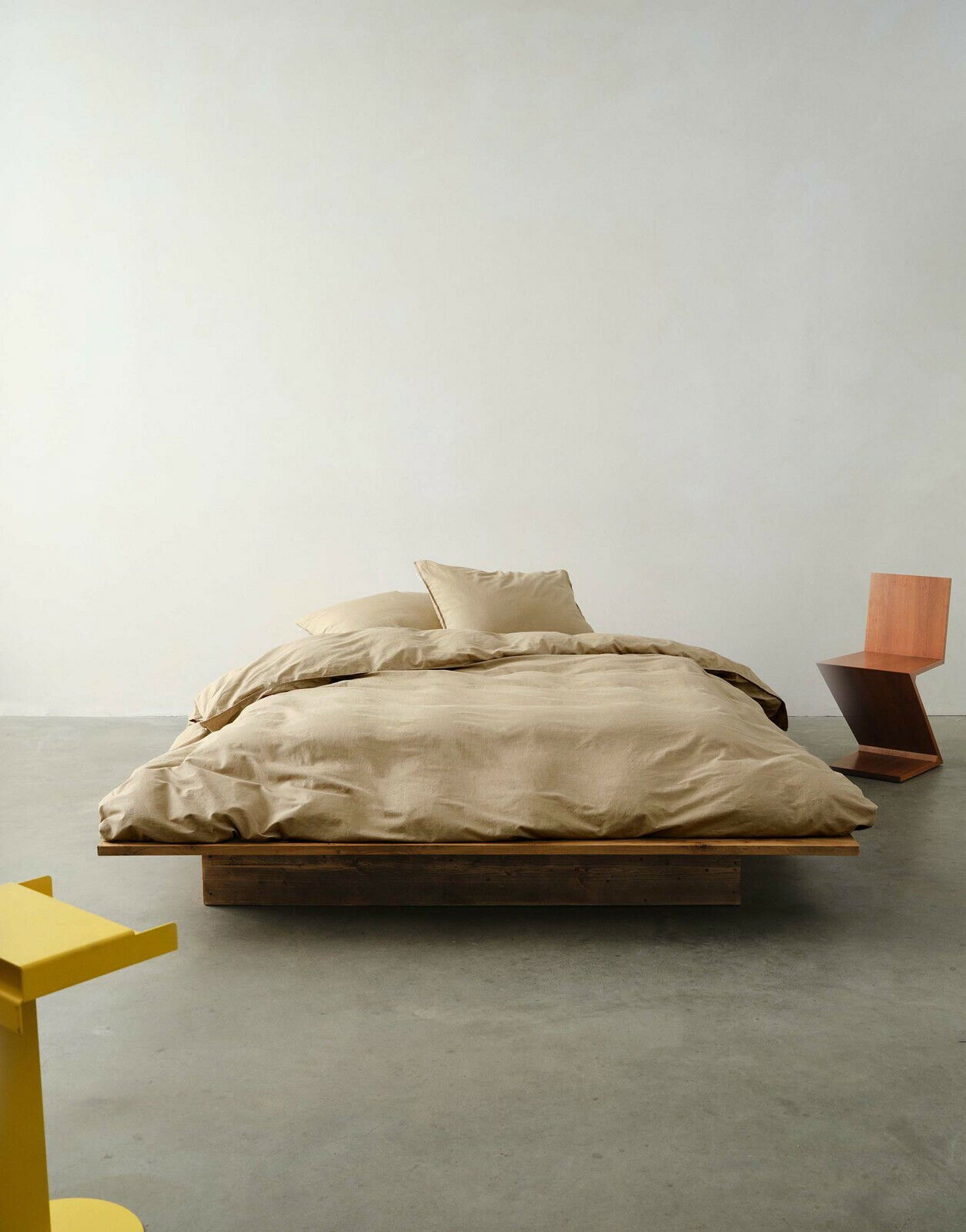 Bett mit beiger Bettwäsche in einem minimalistischen Raum, frontal aufgenommen