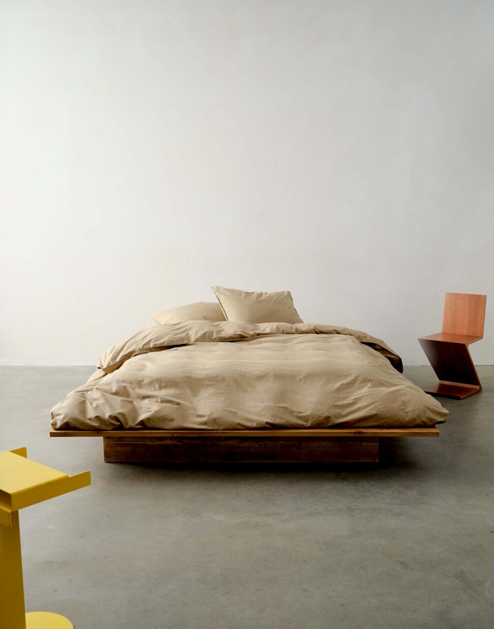 Bett mit beiger Bettwäsche in einem minimalistischen Raum, frontal aufgenommen