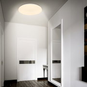 Ronde plafondlamp met warm wit licht in een moderne witte hal, gezien vanuit een laag standpunt omhoog richting het plafond (kikvorsperspectief)
