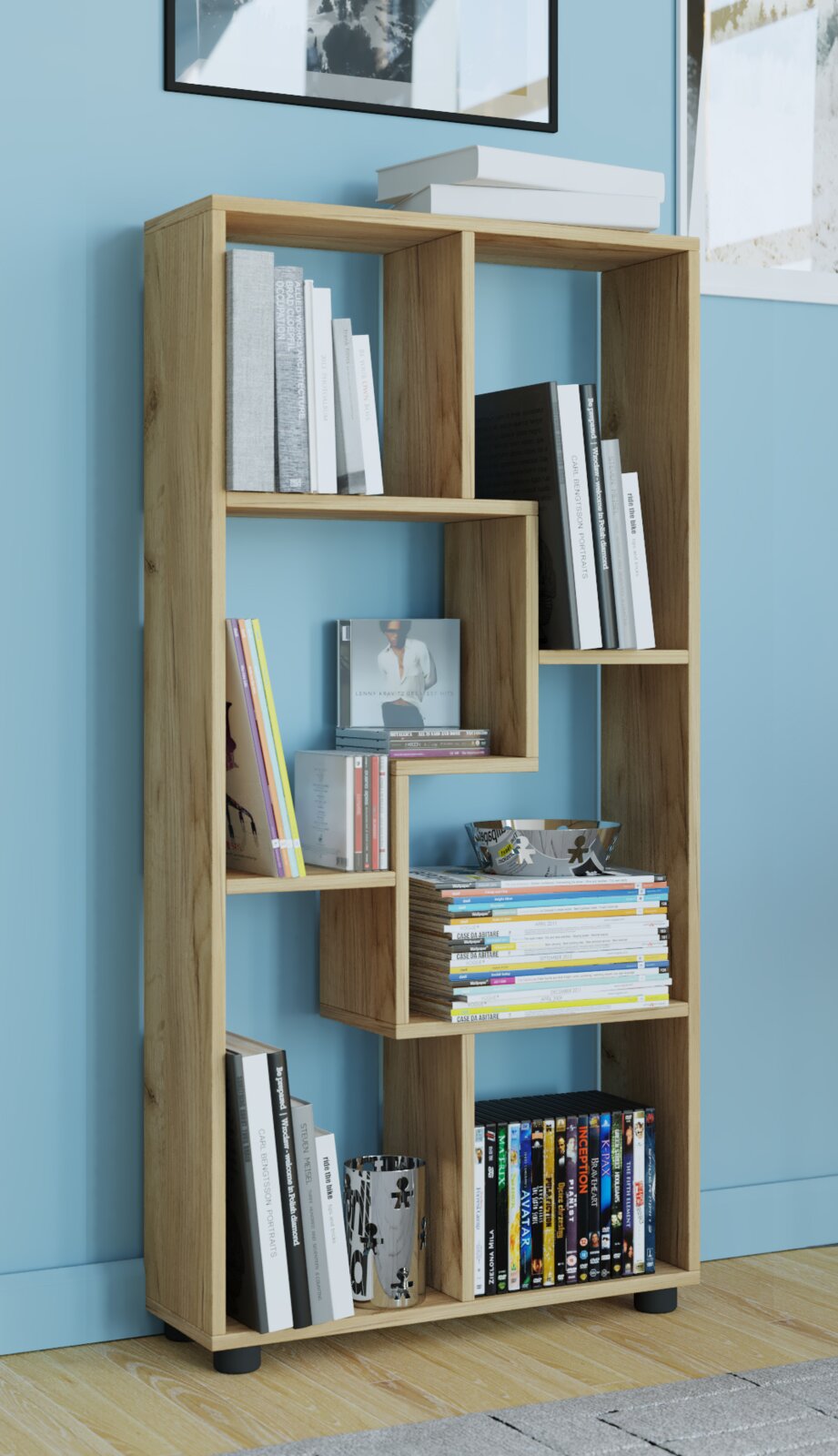 Modernes, asymmetrisches Bücherregal aus hellem Holz mit offenen Fächern, gefüllt mit Büchern, Zeitschriften und Deko; Aufnahme in leichter Schrägansicht von vorn vor blauer Wand.