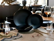 Elegantes schwarzes Geschirrset mit matten Tellern und Schalen, aus leicht erhöhter Frontalperspektive auf einer festlich gedeckten Holztischtafel präsentiert