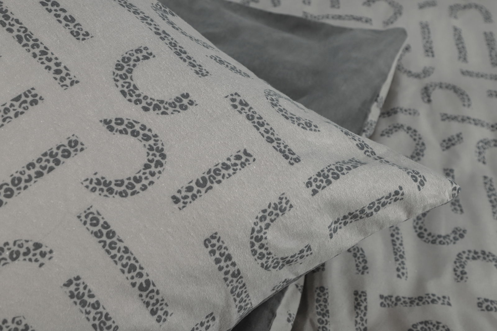 Nahaufnahme von Esprit Bettwäsche mit Leopardenmuster und Buchstaben auf grauem Hintergrund, perspektivisch von oben fotografiert.