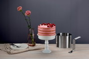 Winkelpalette extra hoch 24cm aus Edelstahl mit weißem Griff, seitlich neben einer Torte auf einem weißen Tortenständer, mit Blumen und Geschirr im Hintergrund.