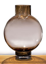 Große, runde Glasvase in Rauchglasoptik, frontal auf einem Holztisch präsentiert.