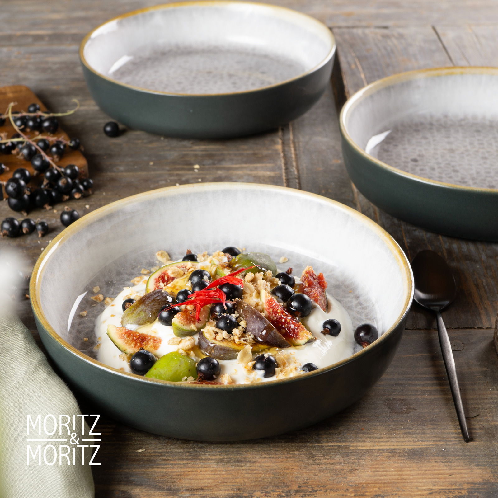 Draufsicht auf ein Moritz & Moritz Geschirrset mit drei grauen Schalen, eine davon gefüllt mit Joghurt, Früchten und Nüssen, auf einem Holztisch.