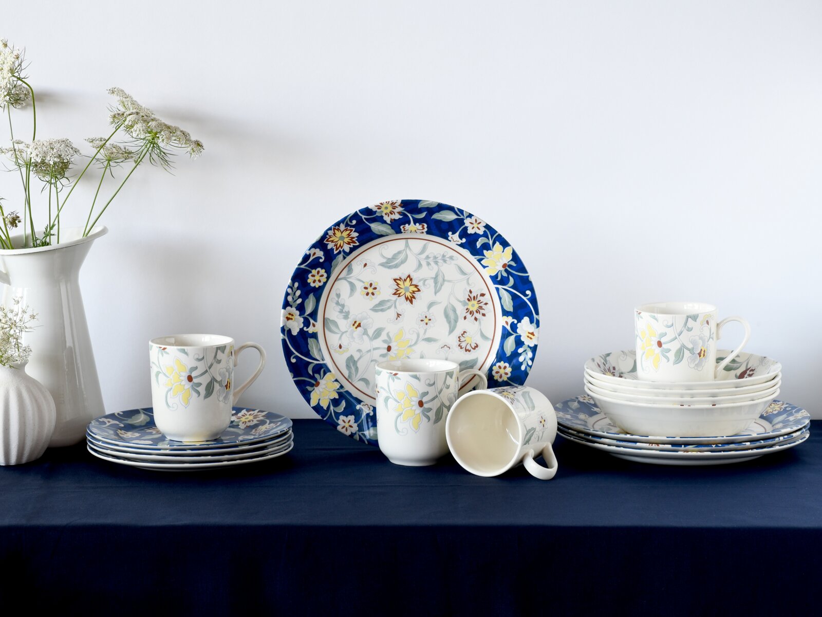 creaTable Kombiservice 16-tlg ODESSA Blau-weißes Porzellan-Geschirrset mit floralem Muster, Teller und Tassen auf dunkelblauem Tuch vor hellem Hintergrund, seitliche Frontansicht