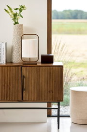 Vooraanzicht van een moderne tafellamp met houten frame en crèmekleurige kap, sfeervol geplaatst op een houten dressoir.