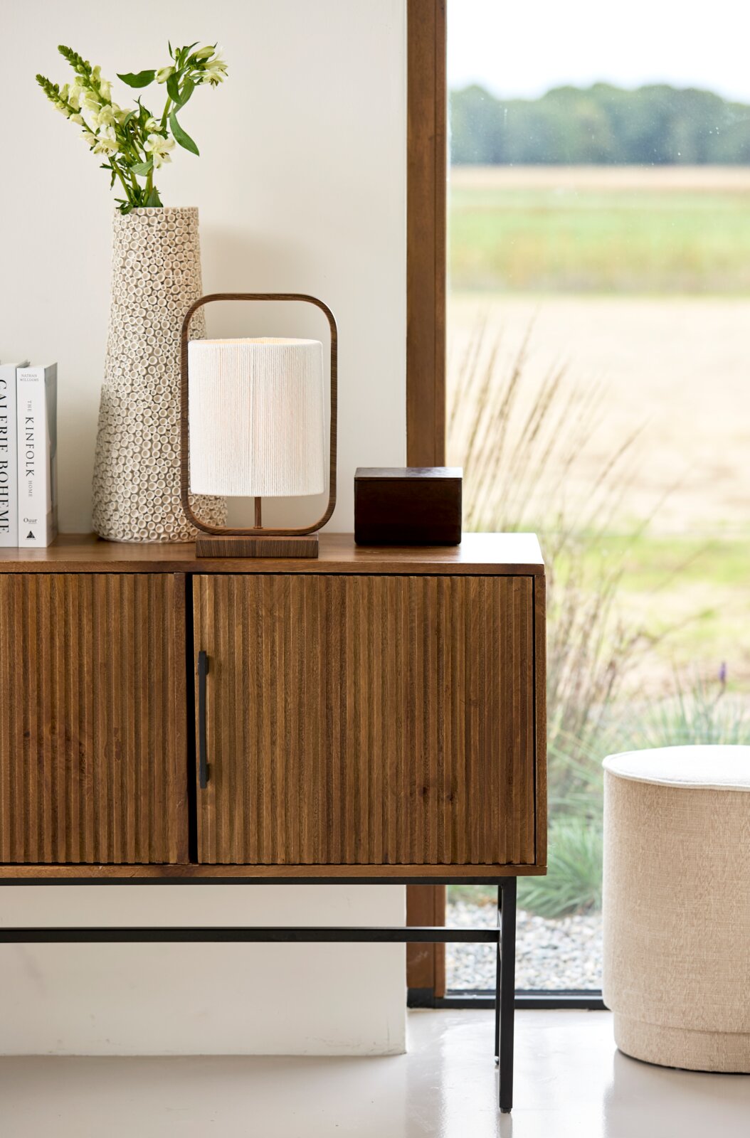 Vooraanzicht van een moderne tafellamp met houten frame en crèmekleurige kap, sfeervol geplaatst op een houten dressoir.