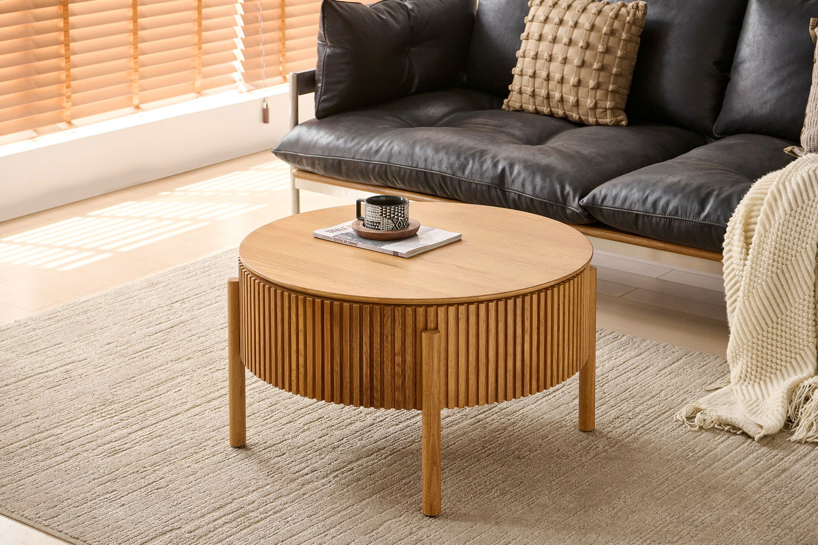 Runder Couchtisch aus Holz mit geriffeltem Design, in einem modernen Wohnzimmer mit schwarzem Sofa und beigem Teppich, seitliche Perspektive
