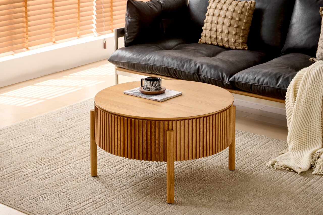 Runder Couchtisch aus Holz mit geriffeltem Design, in einem modernen Wohnzimmer mit schwarzem Sofa und beigem Teppich, seitliche Perspektive