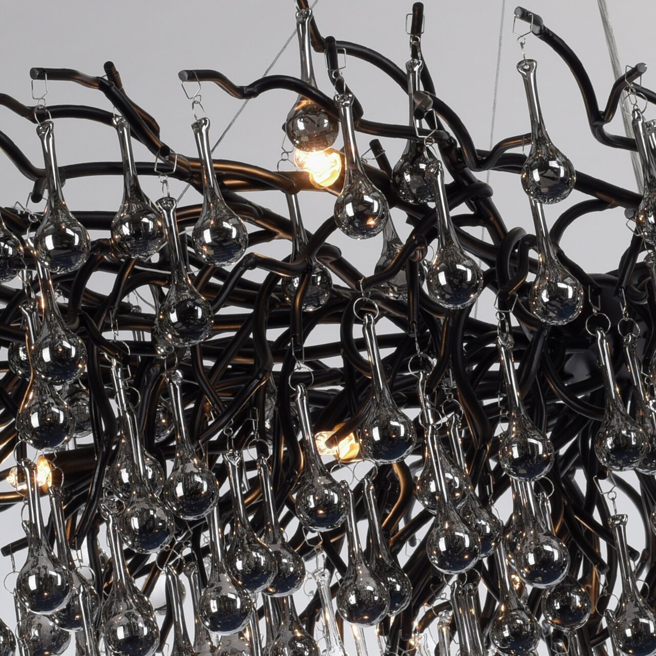 Close-up van een kroonluchter met veel hangende glazen druppels en een complex, zwart metalen frame.