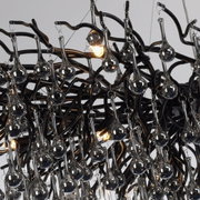 Close-up van een kroonluchter met veel hangende glazen druppels en een complex, zwart metalen frame.