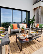 Moderne Loungegarnitur auf einer Terrasse mit grauen Sofas, bunten Kissen und einem Tisch mit Dekorationen, aus der Perspektive von vorne.