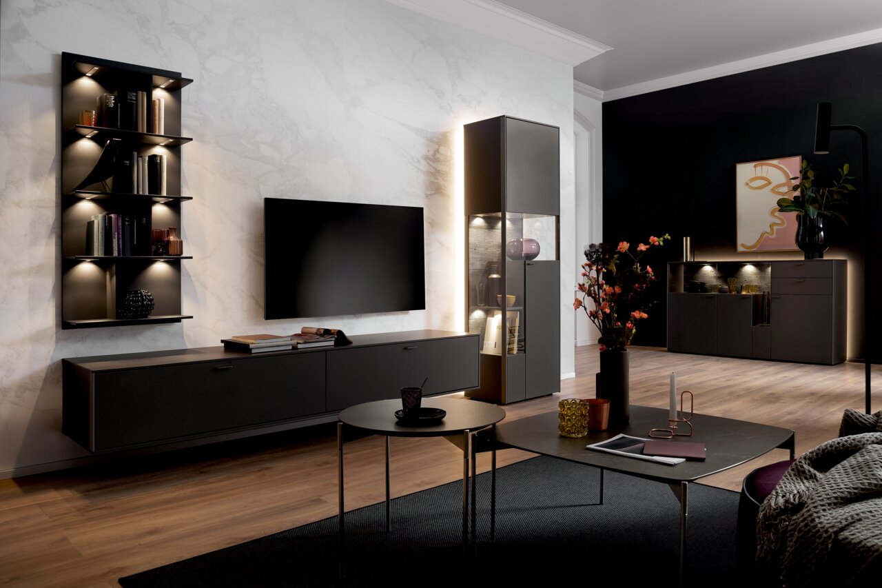 Moderne Wohnzimmer-Wandkombination mit dunklen Schränken, beleuchteten Regalen und einem großen Flachbildfernseher, aus der Perspektive eines gemütlichen Wohnzimmers mit stilvoller Dekoration.